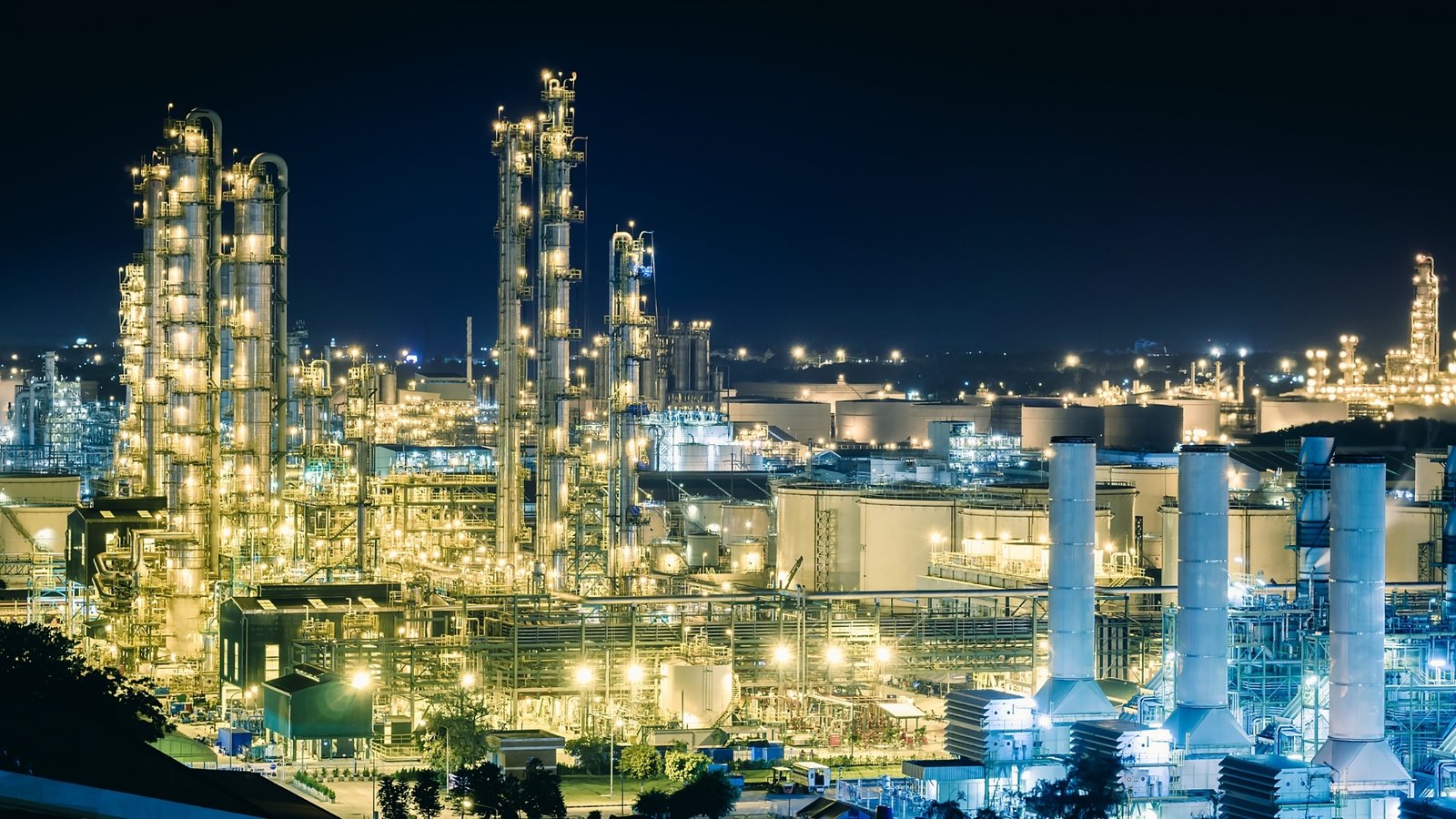 A liquefied natural gas export terminal lit at dusk, storage tanks in the foreground.